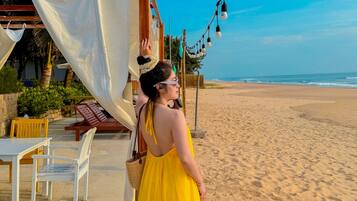 A beachside setting with a wooden pergola, white fabric canopy, and string lights.