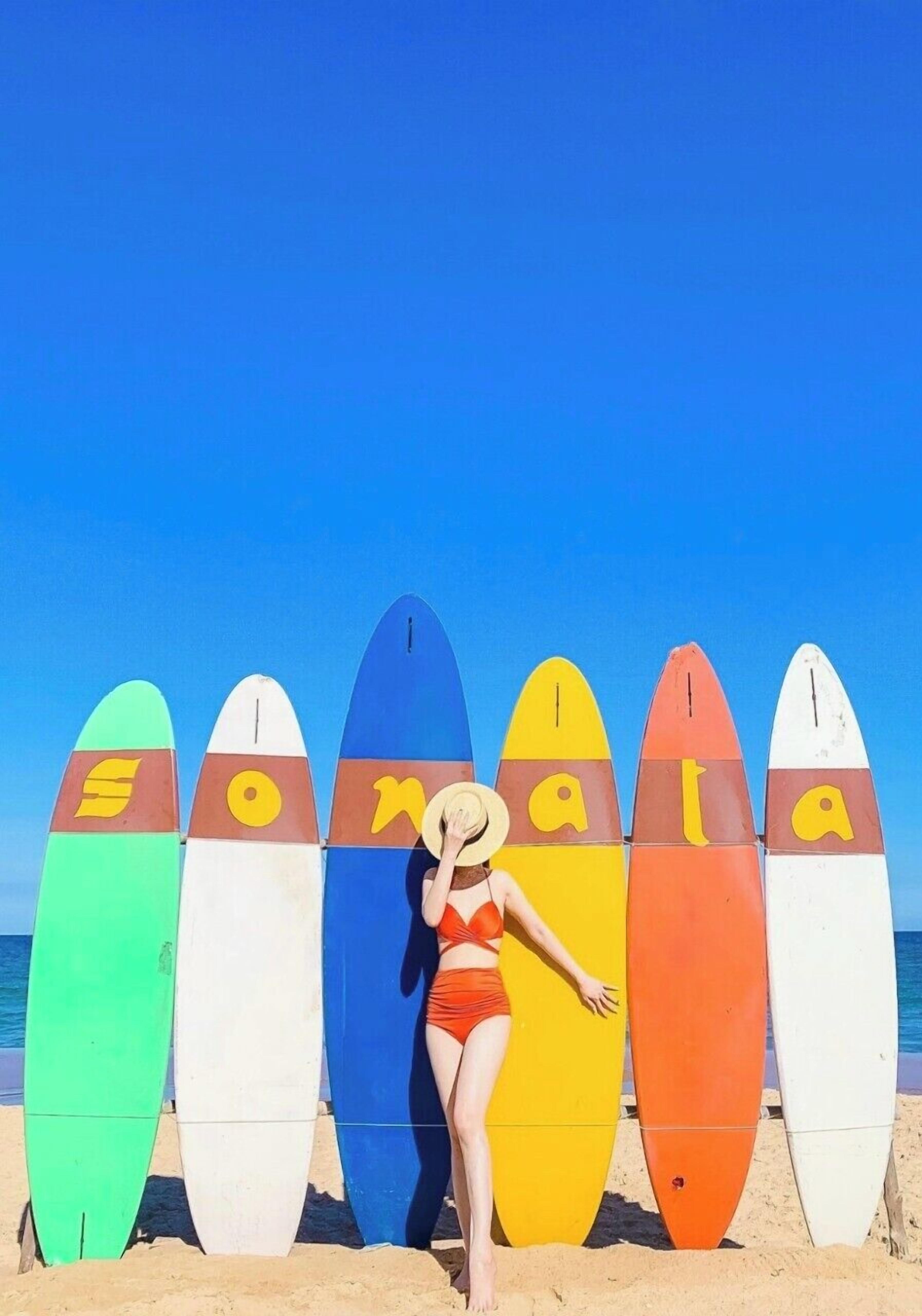 A person standing in front of a row of colorful surfboards on a beach.