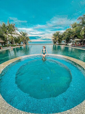 A woman in a swimsuit sitting at the edge of a circular pool with a clear view of the ocean and palm trees in the background. - Sonata Resort & Spa (Tien Thanh)