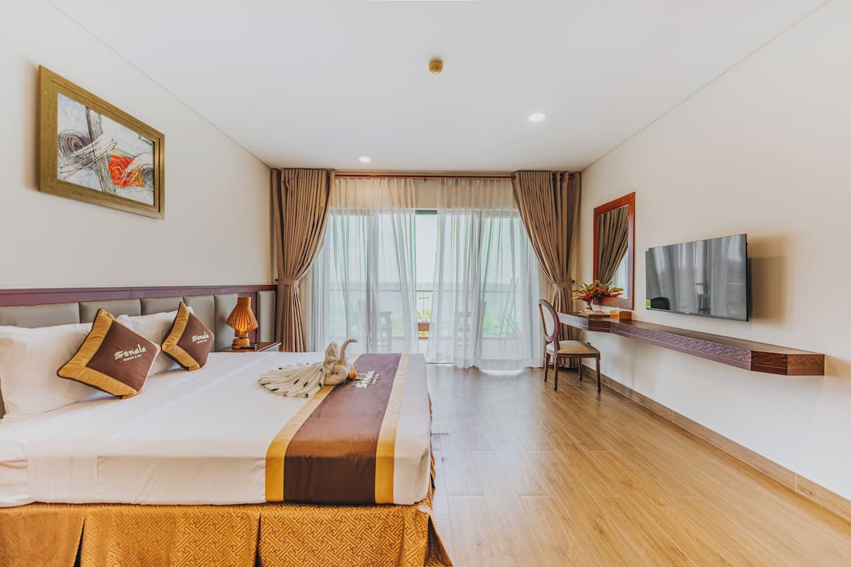 A hotel room with a bed, a desk with a TV, and a window with curtains.