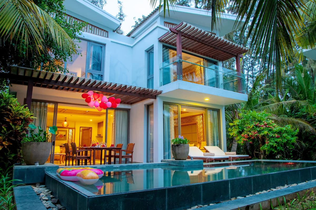 A modern two-story house with a swimming pool, outdoor seating, and lush greenery.