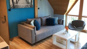 A cozy living room with a sofa, a coffee table, and a chair. There's a painting on the wall and a wooden ceiling. - Penzión Hradby (Prešov)