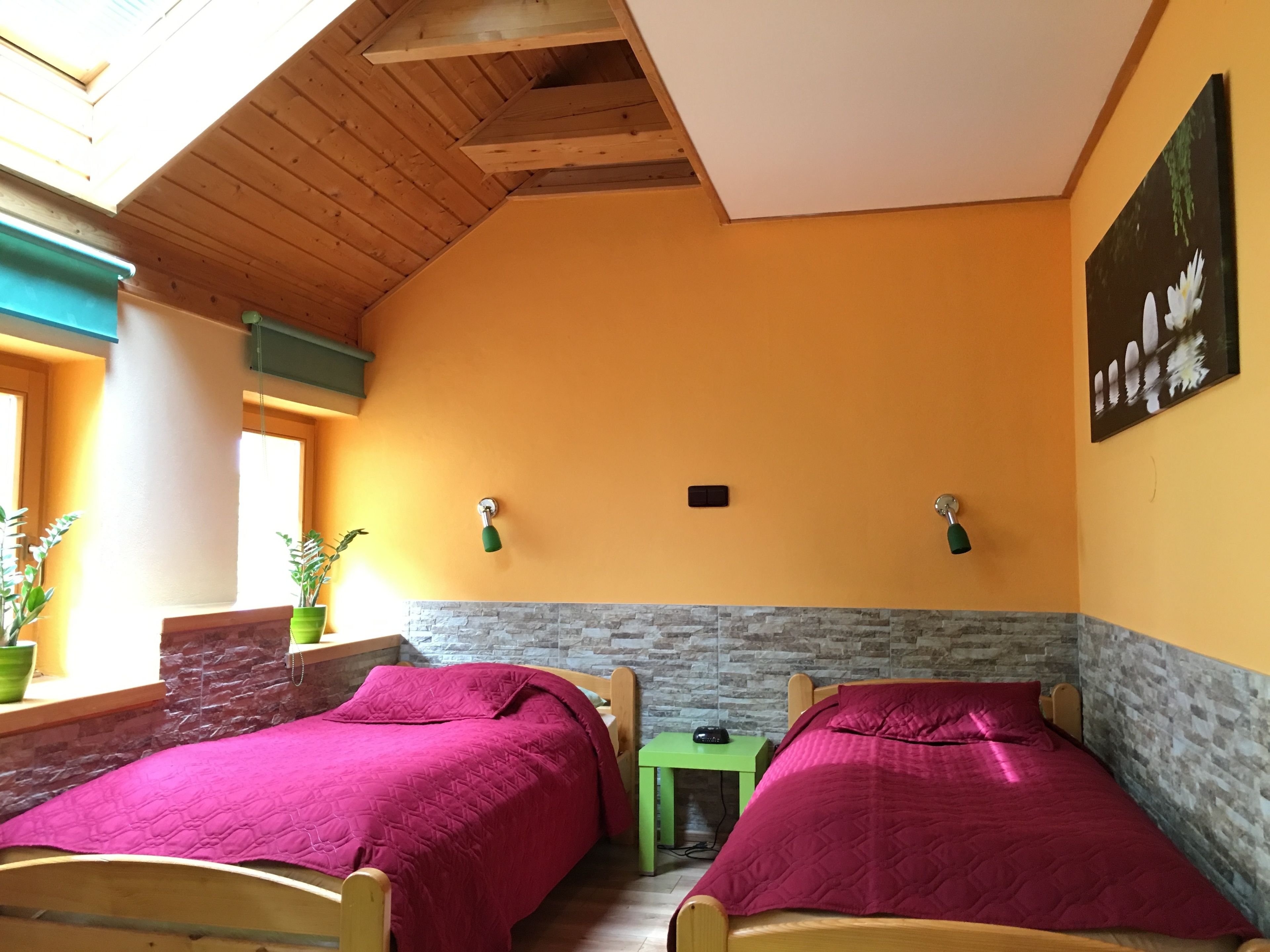 A room with two wooden beds, a stone accent wall, a green side table, and a window with plants.