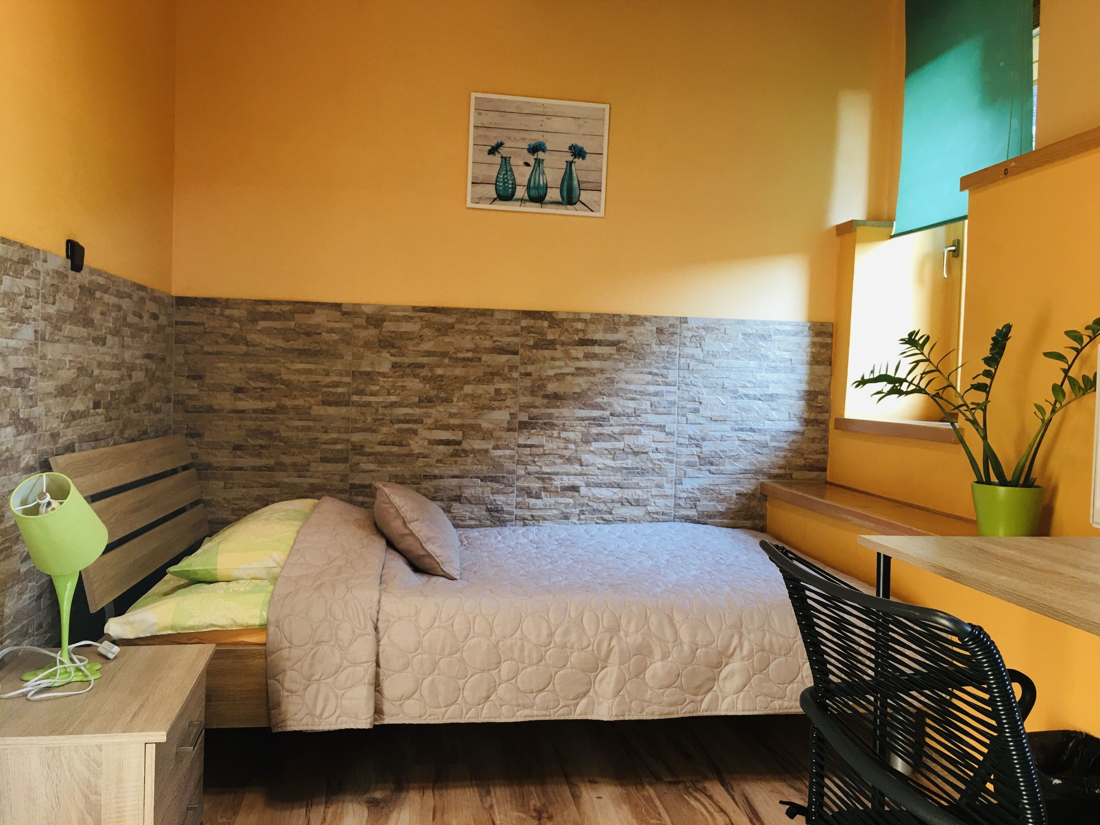 Une chambre à coucher comprenant un lit, un banc, un bureau, une plante verte et une œuvre d’art accrochée au mur.