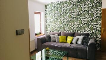 A living room with a grey sofa, a glass coffee table, and a window with curtains.