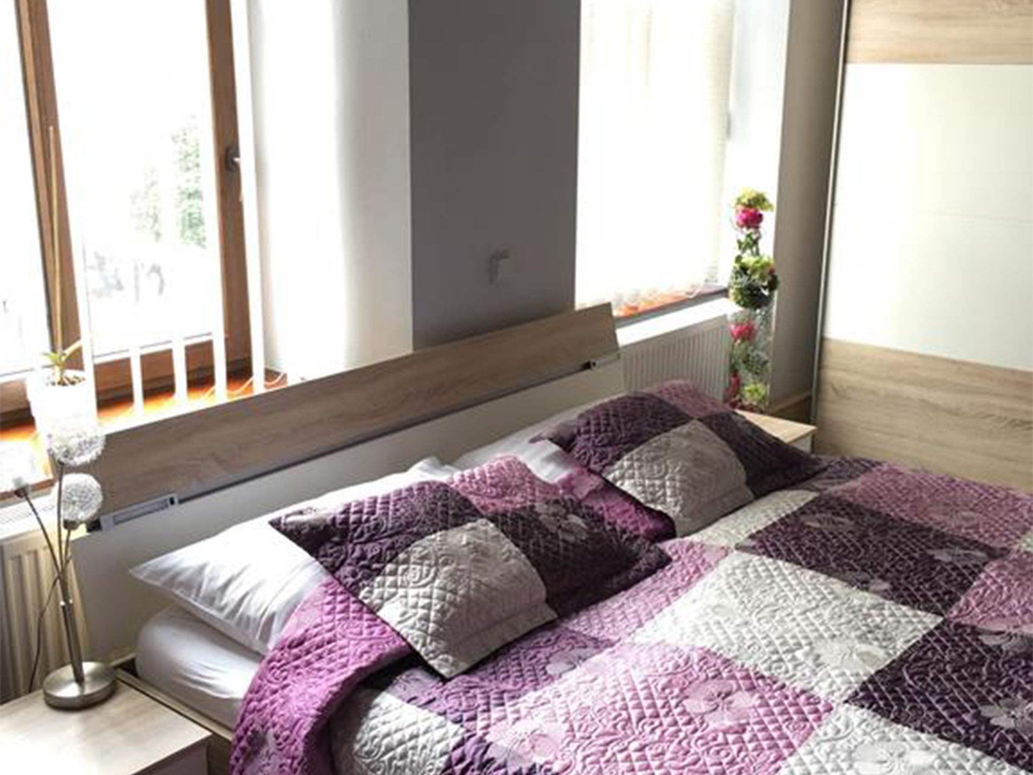 A bedroom with a bed, a bedside table, a lamp, and a window with curtains.