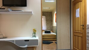 A hotel room with a bed, a bedside table, a TV, and a wooden door. - Penzión Hradby (Prešov)