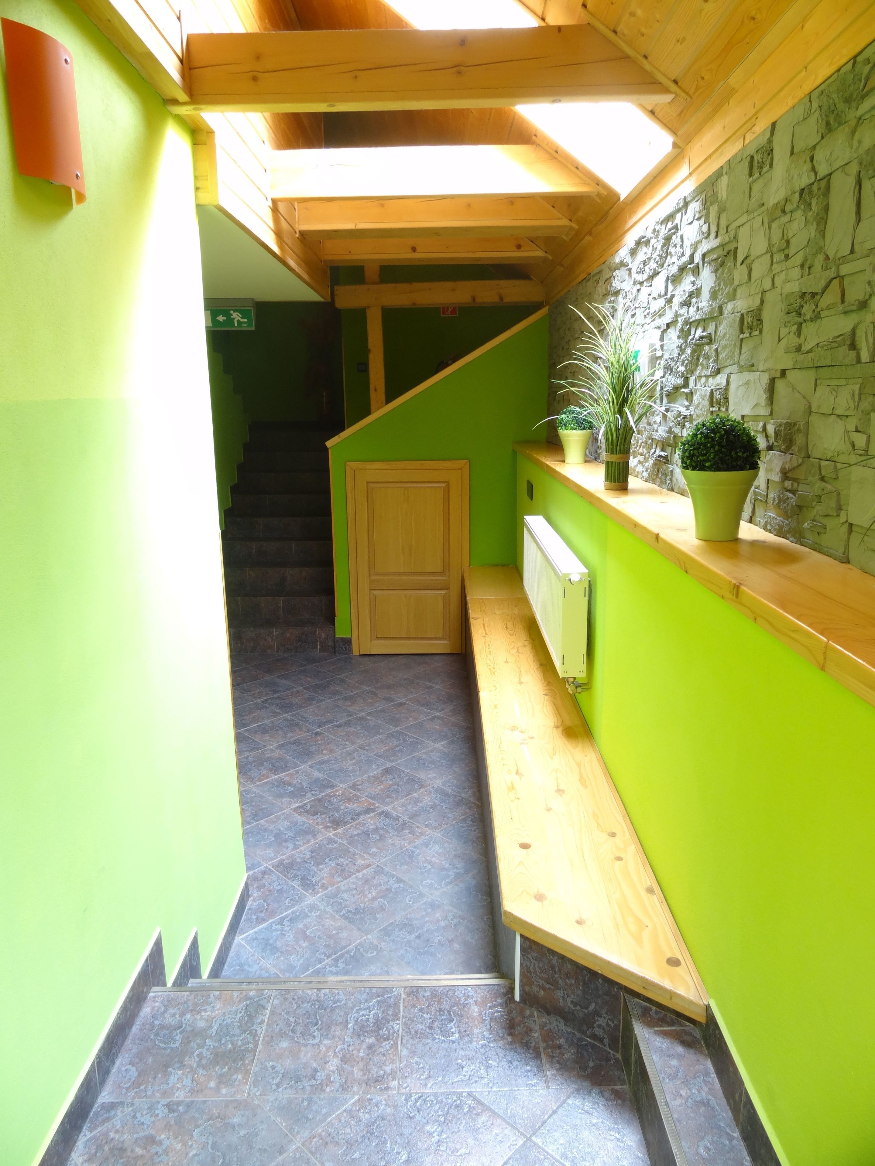 Un pasillo estrecho con una escalera de madera, paredes verdes y una pared de piedra.