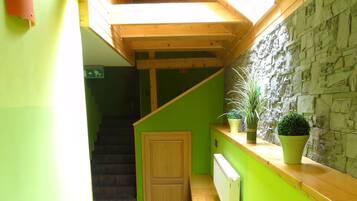 Un pasillo estrecho con una escalera de madera, paredes verdes y una pared de piedra.