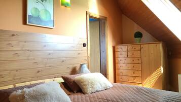 A bedroom with a wooden headboard, a bed with a quilted cover, fluffy pillows, a dresser, and a wall-mounted light fixture.