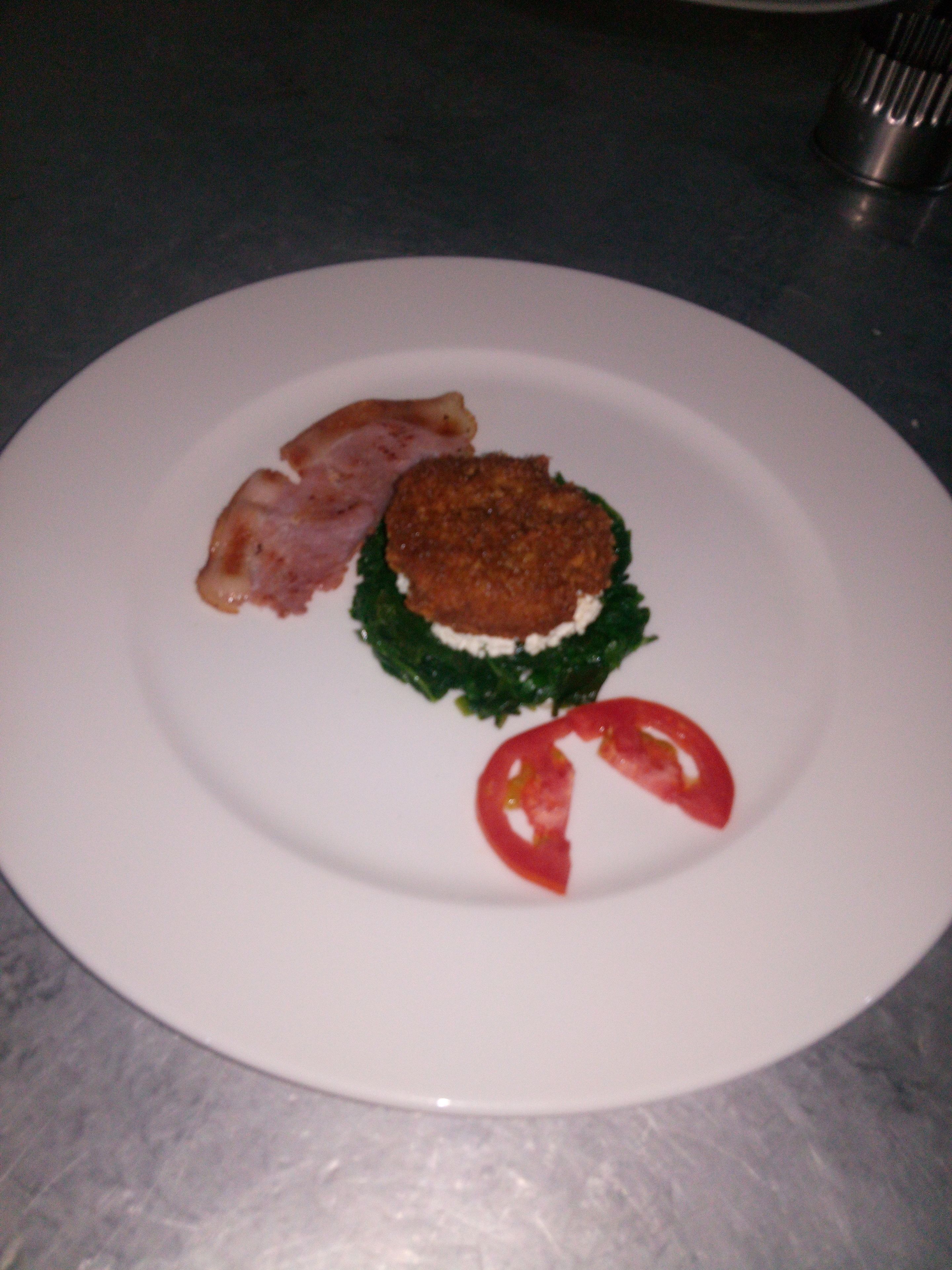 Un plato blanco con una hamburguesa, una rodaja de tomate y una hoja verde sobre una encimera oscura.