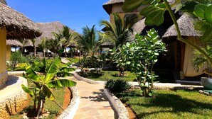 A tropical resort with thatched-roof structures, a paved pathway, and lush greenery. - Mawe Resort Watamu Boutique Hotel (Watamu)