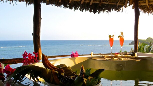 A tropical setting with a pool, a table with fruits and flowers, and two cocktails with umbrellas. - Mawe Resort Watamu Boutique Hotel (Watamu)