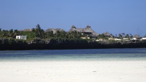 A beachfront property with thatched-roof structures, a sandy beach, and a clear blue sky. - Mawe Resort Watamu Boutique Hotel (Watamu)
