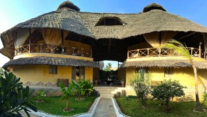 A traditional thatched-roof house with multiple balconies and a stone pathway leading to the entrance. - Mawe Resort Watamu Boutique Hotel (Watamu)