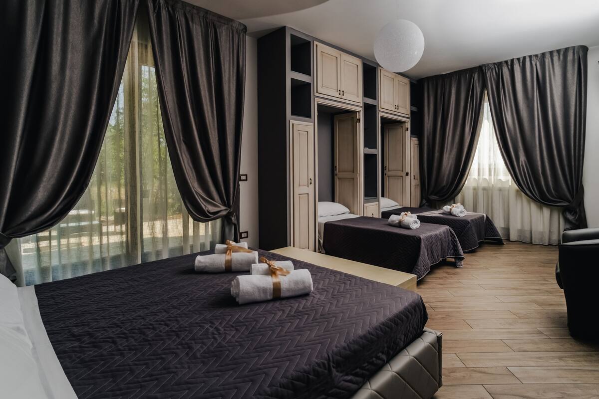 A hotel room with two beds, a sofa, a wardrobe, and a large window with curtains.