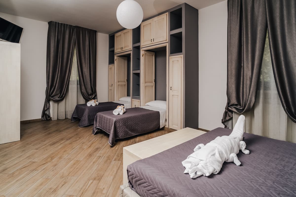A hotel room with two single beds, a large wardrobe, and a large window with curtains.