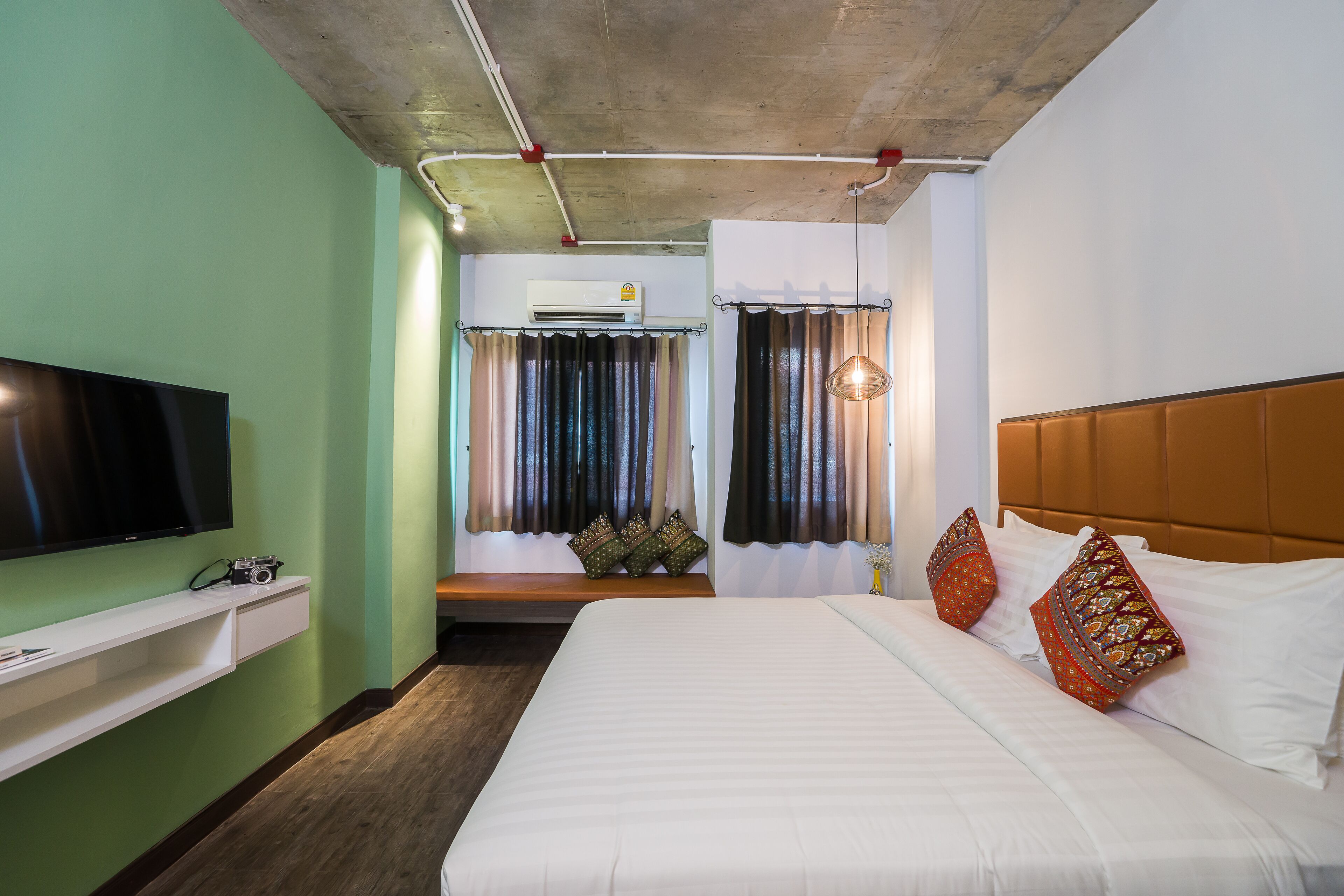 A hotel room with a bed, a TV, a bench, and a window with curtains.