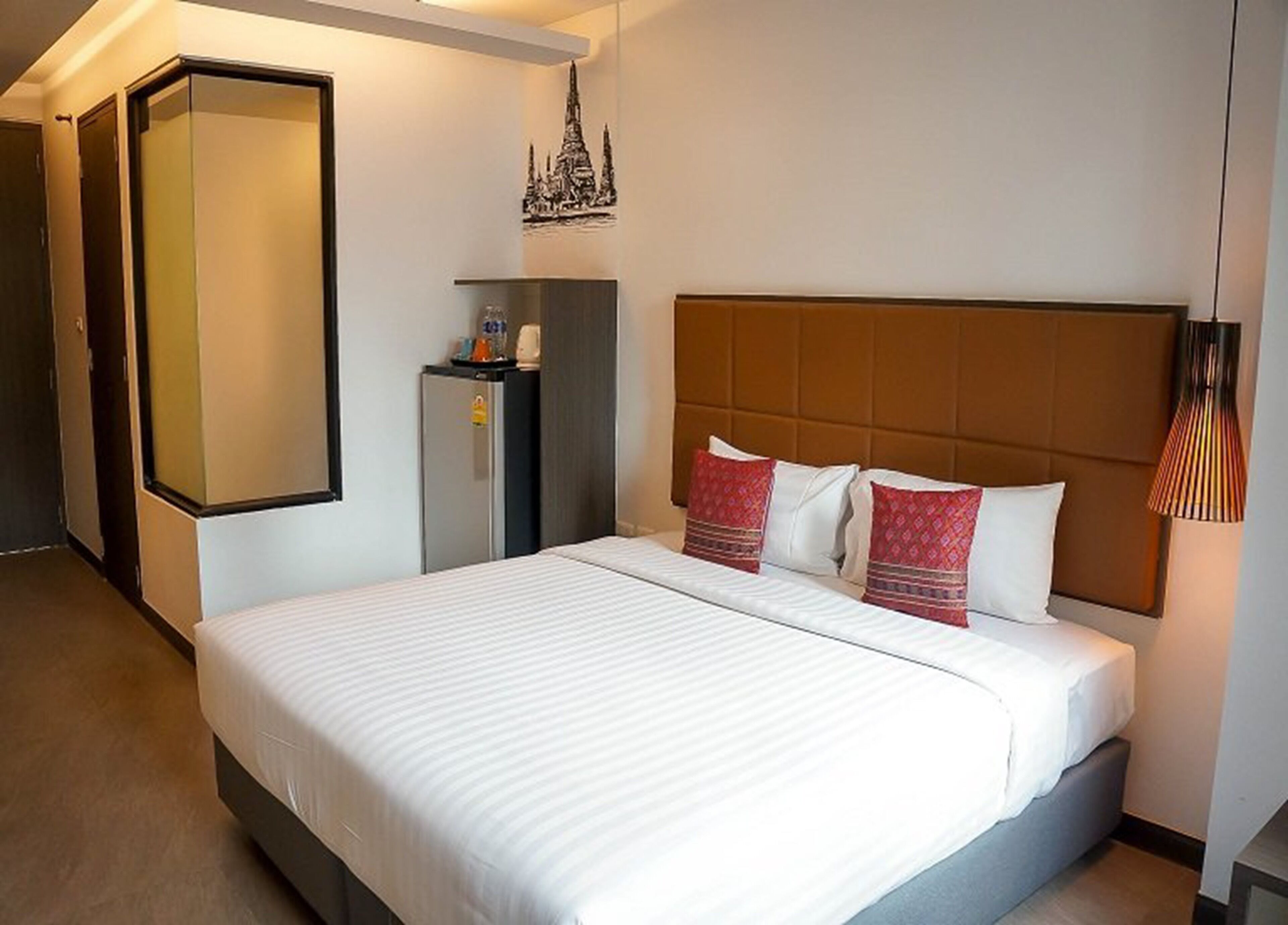 A hotel room with a bed, a wardrobe, a minibar, and a decorative wall piece.