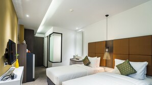 Habitación de hotel con dos camas, un escritorio con espejo, televisor y baño con ducha e inodoro.