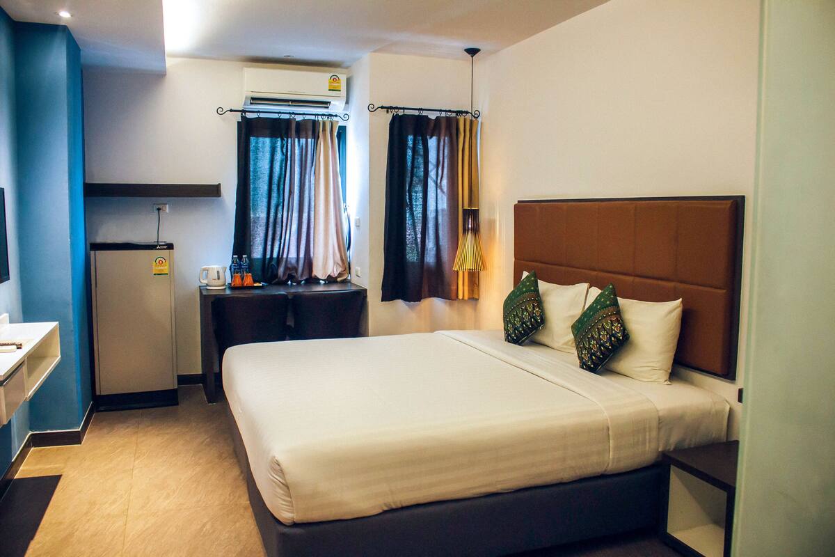 Een hotelkamer met een bed, een bureau, een koelkast en een raam met gordijnen.
