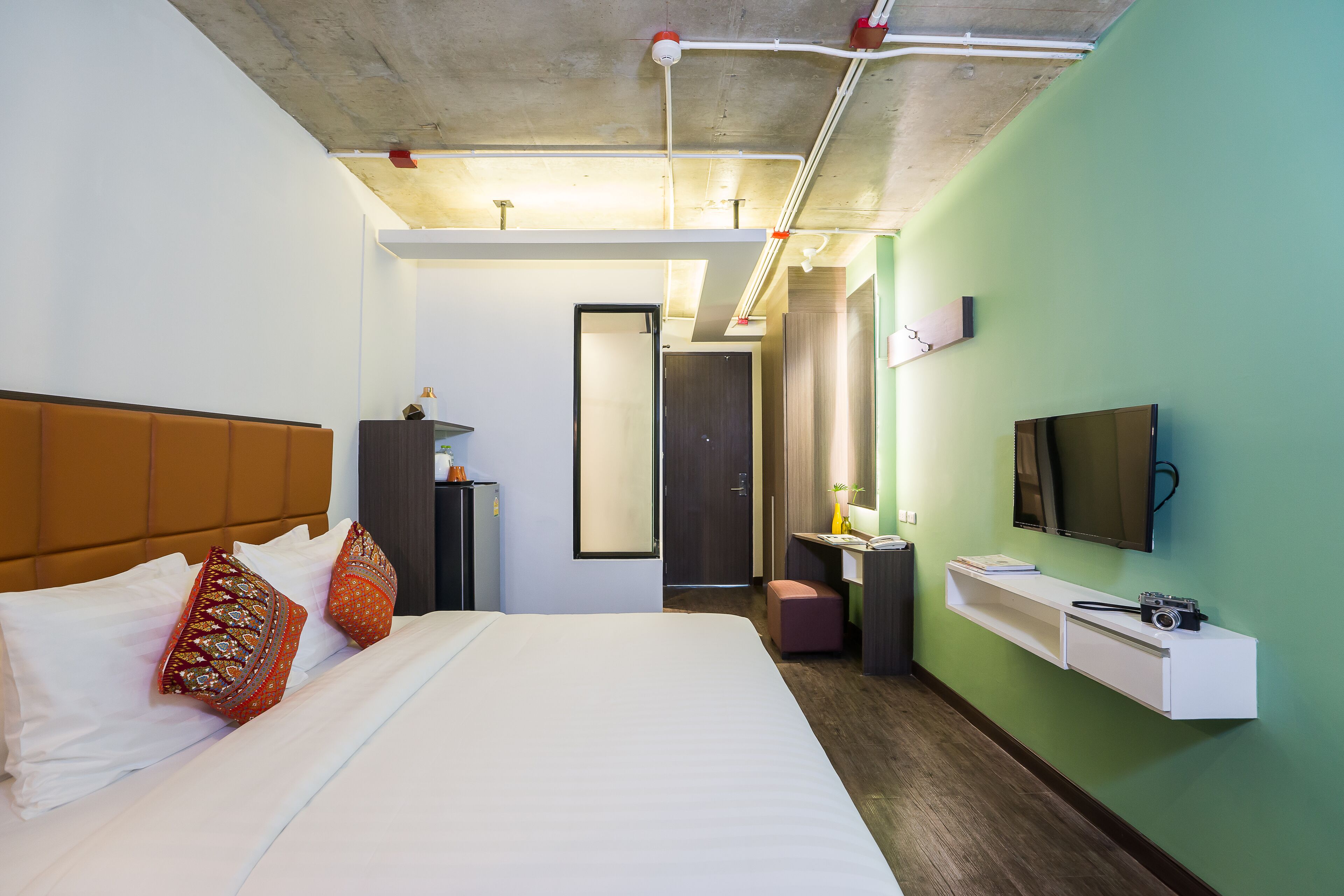 A hotel room with a large bed, a desk with a chair, a television, and a mirror.