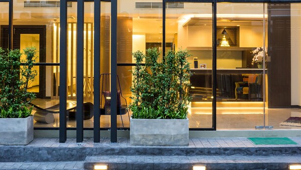 Un edificio moderno con amplios ventanales de vidrio, un interior luminoso y un área de entrada pavimentada con jardineras.