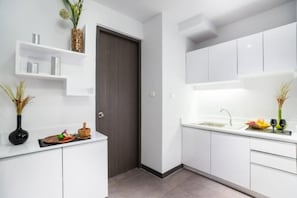 Una cocina moderna con armarios blancos, una puerta oscura y una encimera con un lavabo y objetos decorativos.
