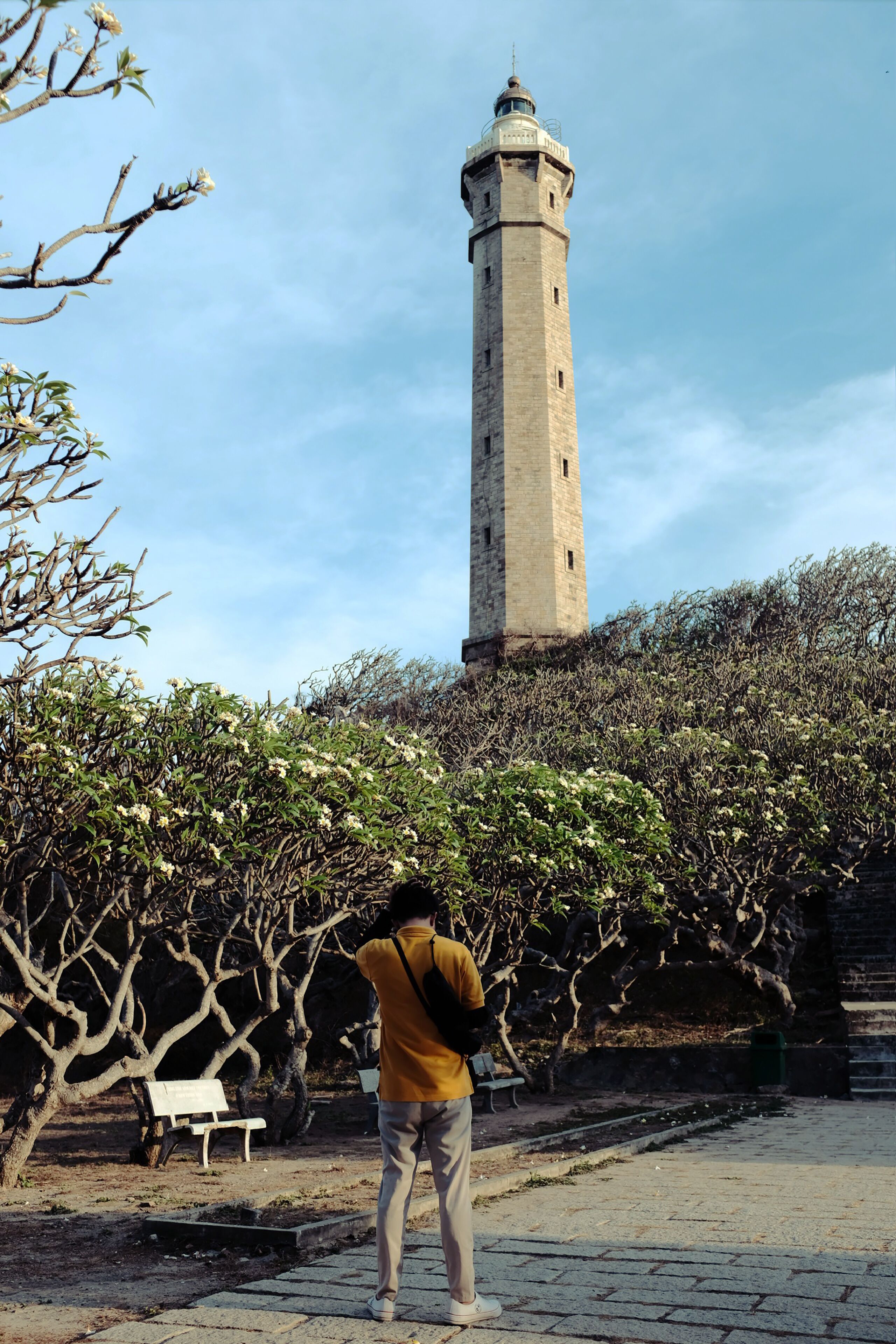 Une personne se tient dans un parc, avec un phare en arrière-plan.