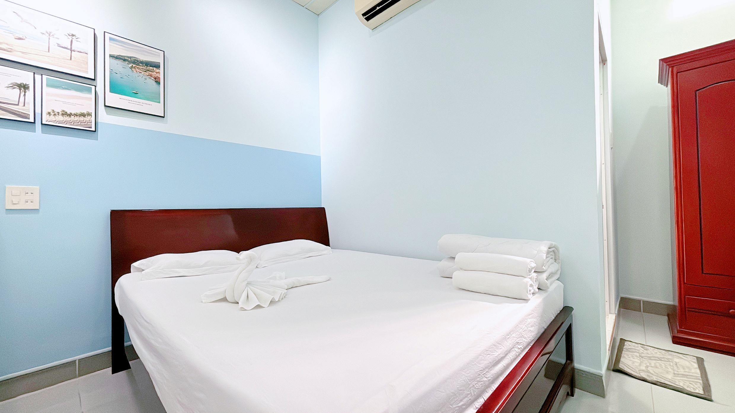 Una cama bien hecha con sábanas y toallas blancas, cabecera de madera y una pared decorada con cuadros.