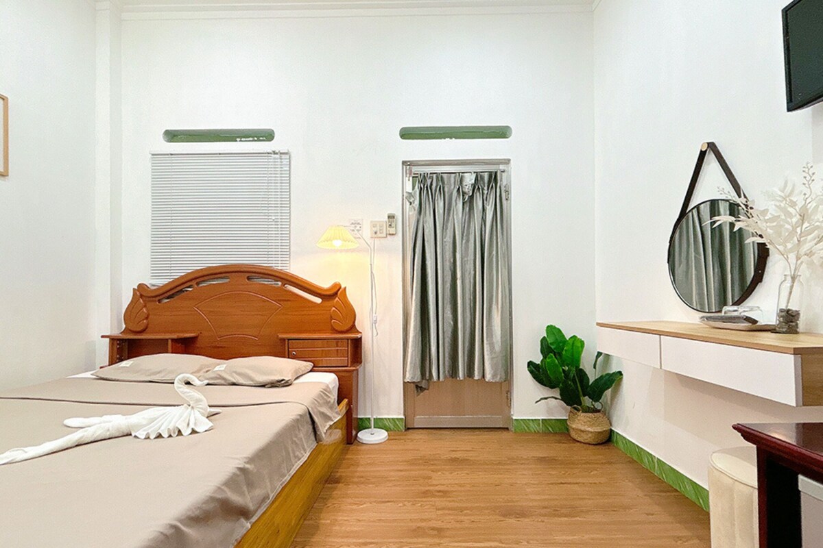 A hotel room with a wooden bed, a bedside lamp, a potted plant, a mirror, and a television mounted on the wall.