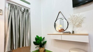 A room with a wooden floor, a green plant, a mirror, a television, and a small table with a vase.
