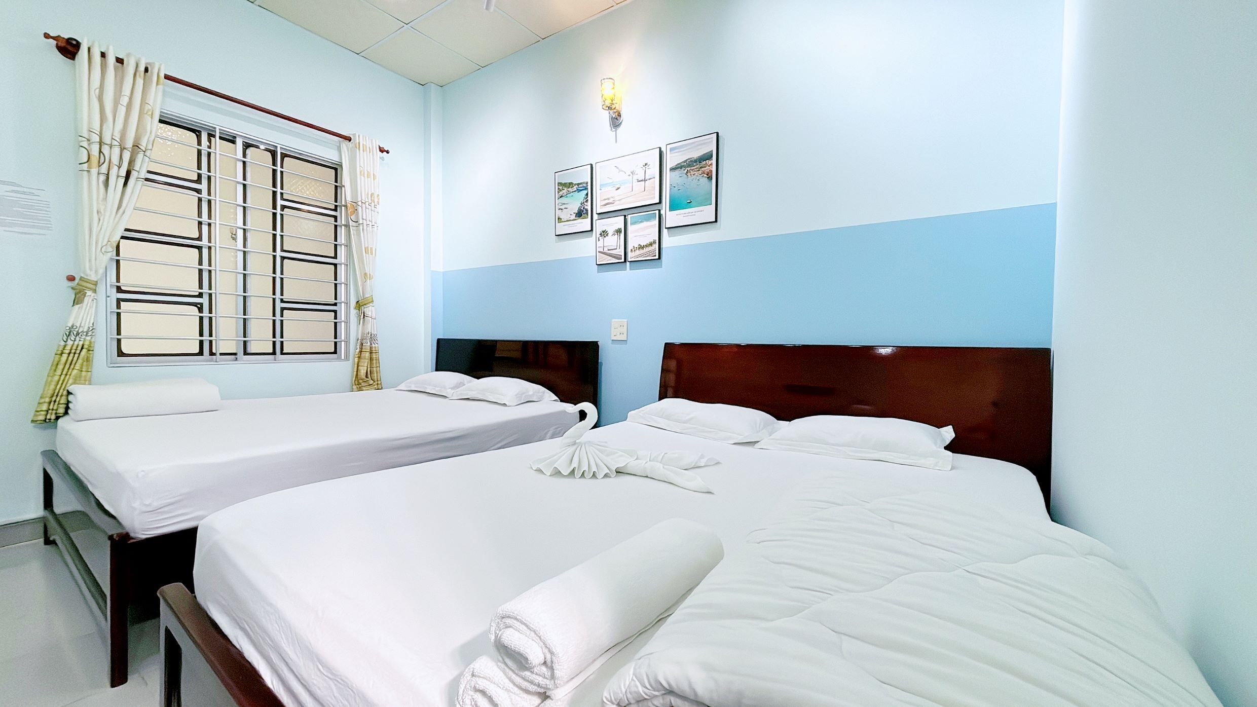 A hotel room with two beds, a window with curtains, and wall-mounted pictures.