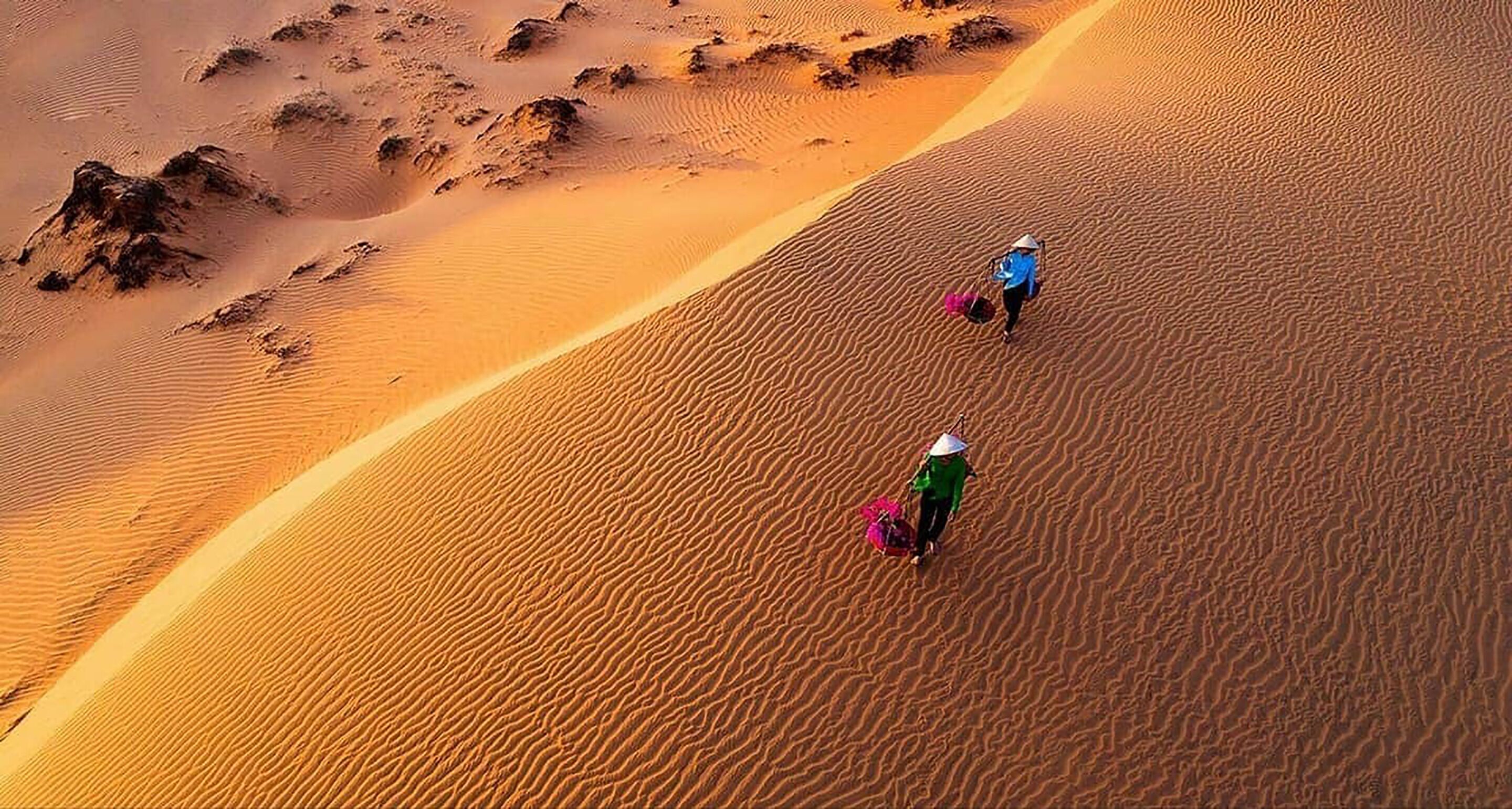 Woestijnlandschap met twee personen die over een zandduin lopen.