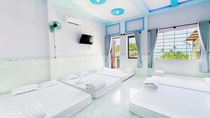 A hotel room with four beds arranged in a U-shape, a flat-screen TV on the wall, and a large window with curtains.