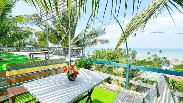 A patio with a table and chairs, surrounded by palm trees and a view of the ocean.