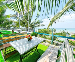A patio with a table and chairs, surrounded by palm trees and a view of the ocean.