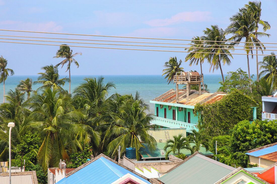 A coastal view with a turquoise building, palm trees, and a clear blue sky.