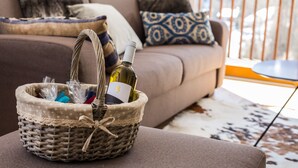 Una cesta de mimbre con una botella de vino y bolsas de plástico sobre un reposapiés acolchado.