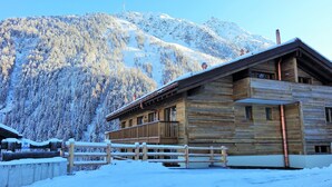 Una cabaña de madera con balcón, rodeada de montañas nevadas.