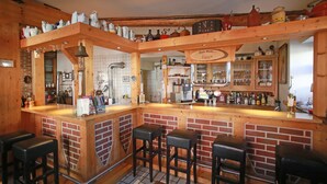 Un área de bar rústica con taburetes de madera, pared de ladrillo y estanterías con botellas y vasos.