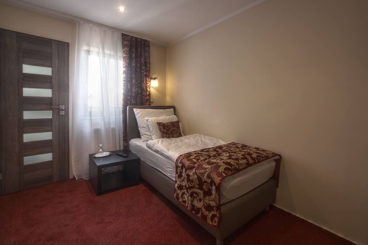 Un dormitorio con cama, mesita de noche, lámpara, puerta y ventana con cortinas.