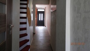 Un pasillo con una escalera de madera, una puerta negra al final y un muro con textura.
