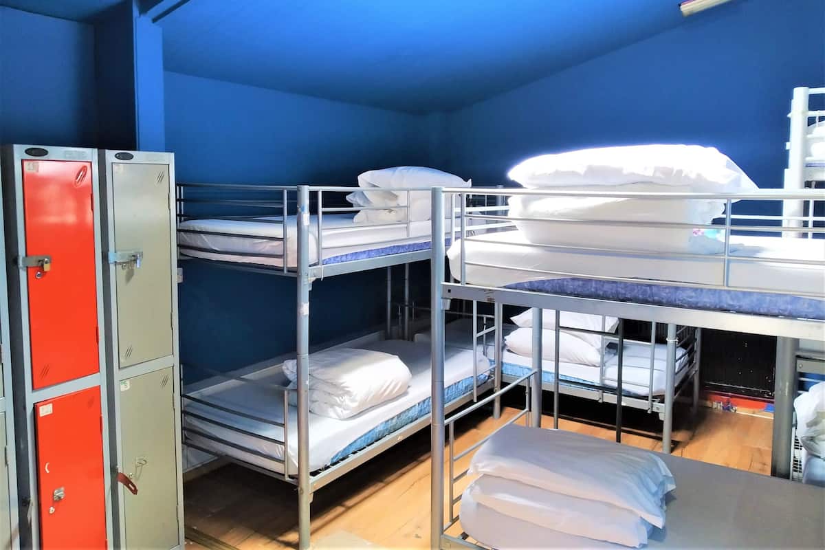 Une chambre de dortoir avec des lits superposés, un meuble de rangement rouge et un mur bleu.