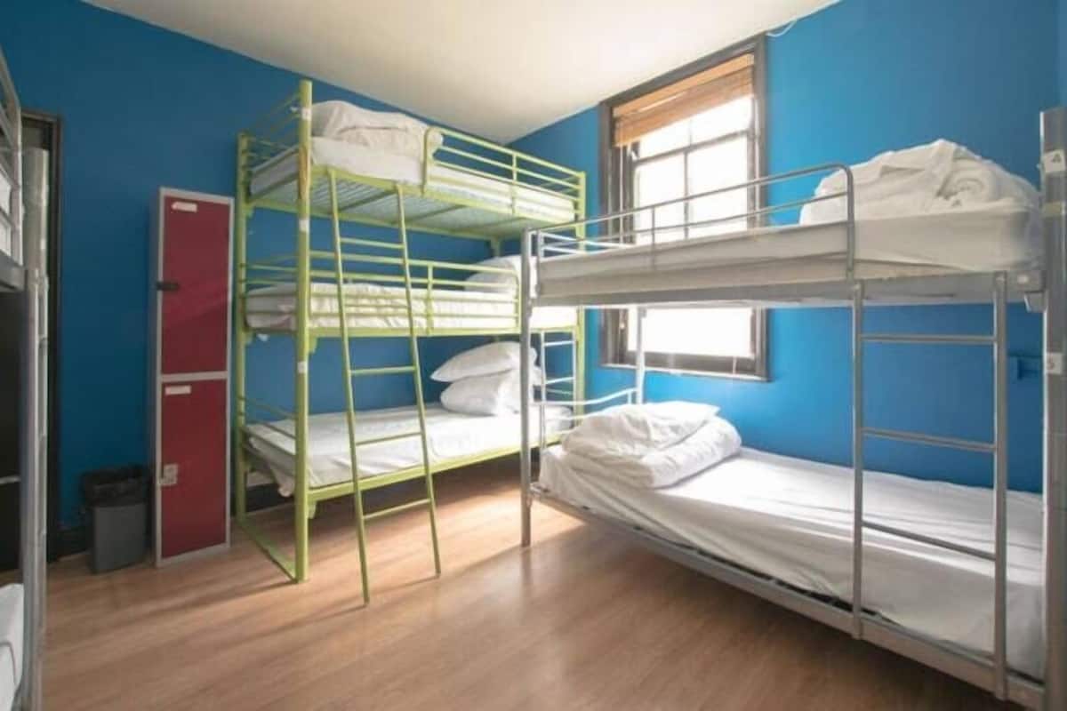 Une chambre de dortoir avec des lits superposés, une armoire rouge et une fenêtre.