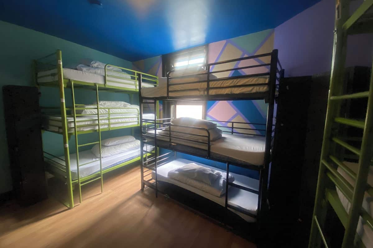 Une chambre de dortoir avec des lits superposés, un plancher en bois et un mur orné d’un motif géométrique.