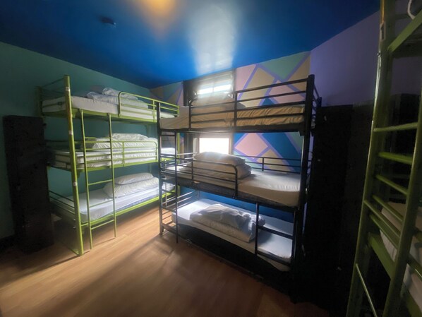 Une chambre de dortoir avec des lits superposés, un plancher en bois et un mur orné d’un motif géométrique.