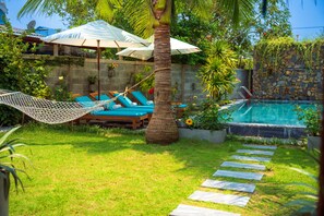 A pool area with a hammock, lounge chairs, and a stone wall. - An Bang Garden Homestay (Da Nang)