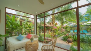 A spacious room with a large sliding glass door leading to a lush garden, a comfortable sofa with cushions, and a wicker coffee table. - An Bang Garden Homestay (Da Nang)