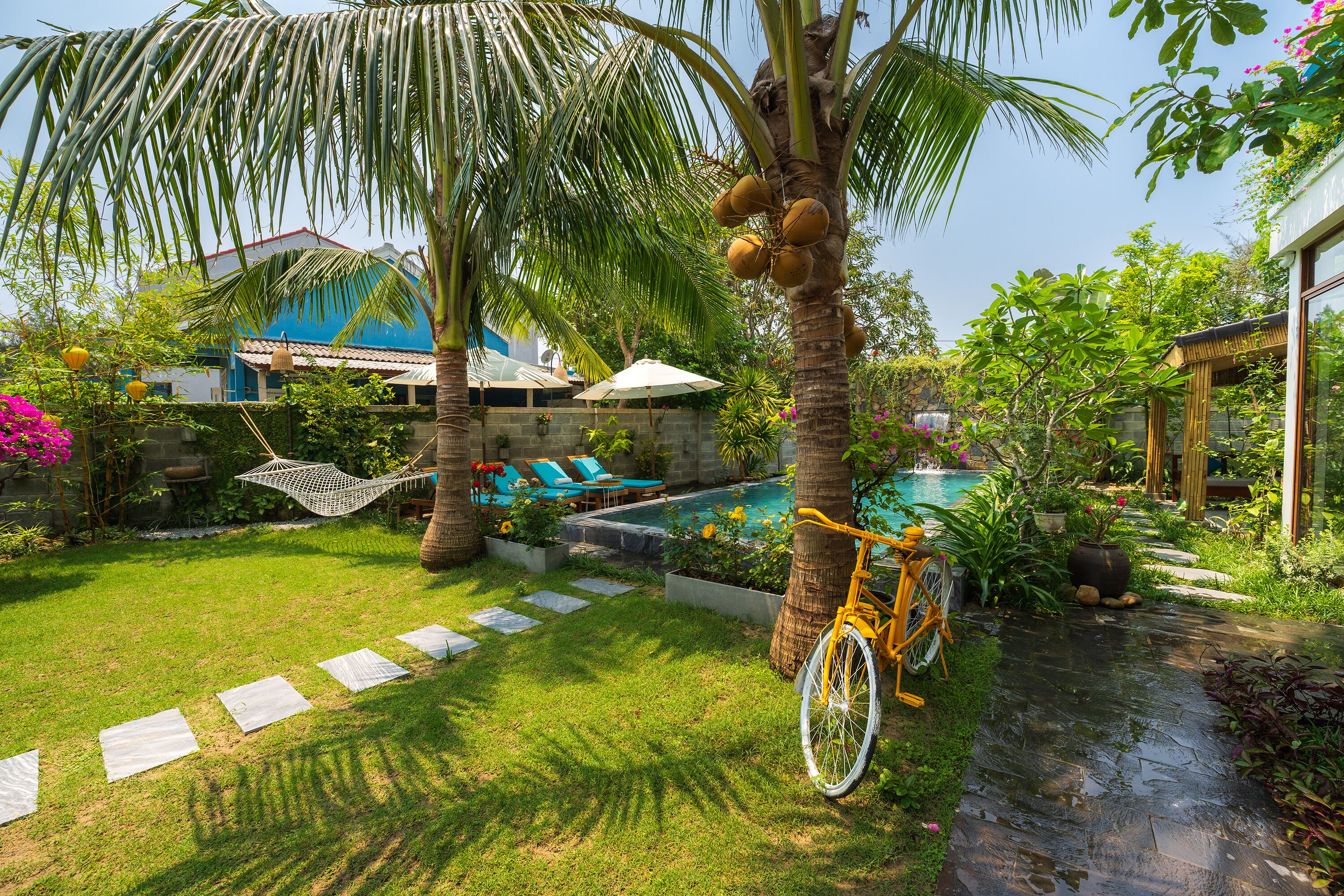 Un patio trasero con piscina, palmeras, una hamaca y una bicicleta.